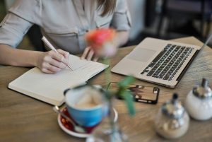 Girl writing on a book with a laptop near it